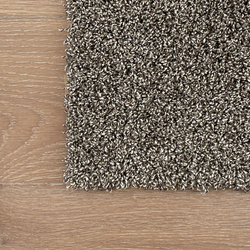 Textured brown carpet sample on a wooden floor. Residential DIY machine washable carpet tle