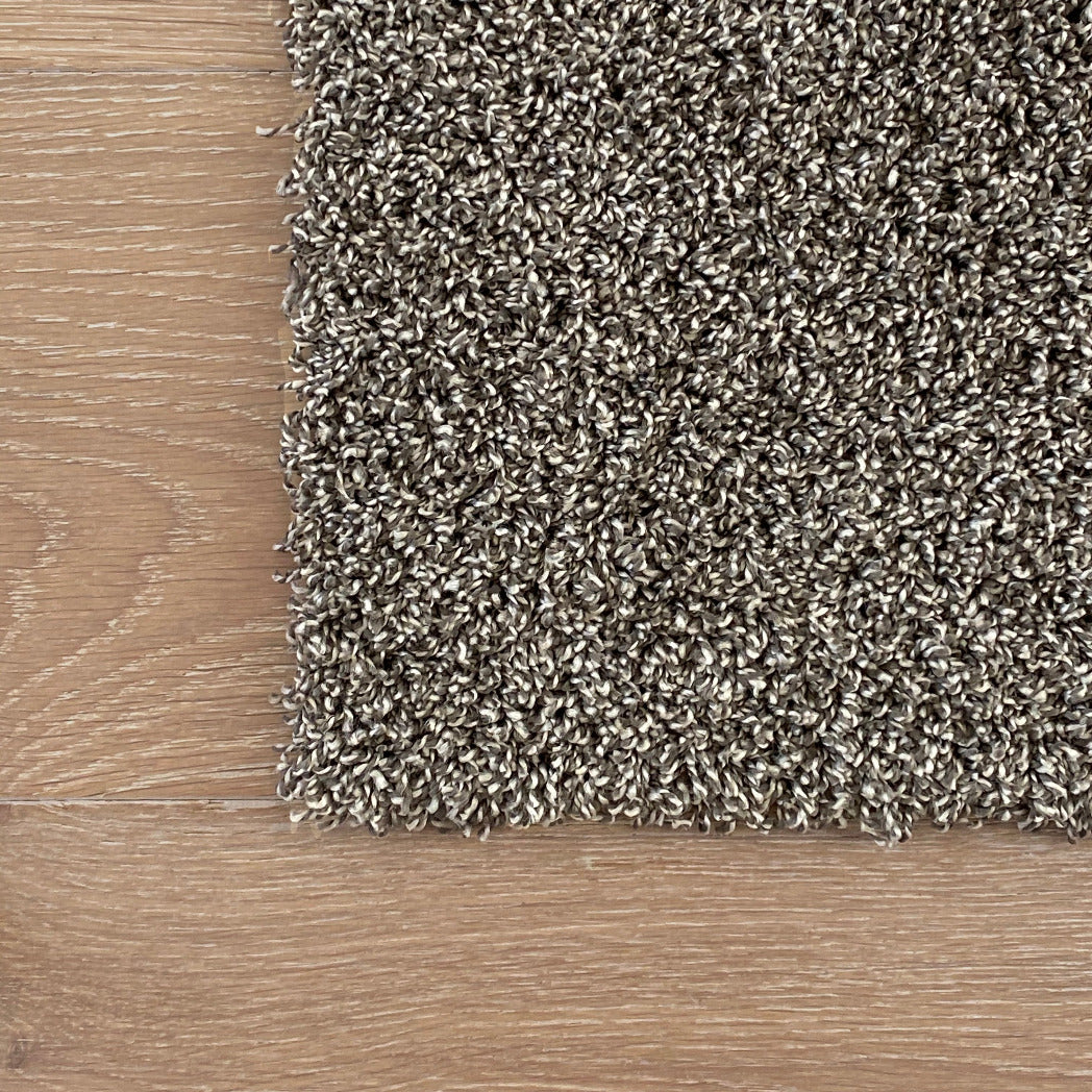 Textured brown carpet sample on a wooden floor. Residential DIY machine washable carpet tle