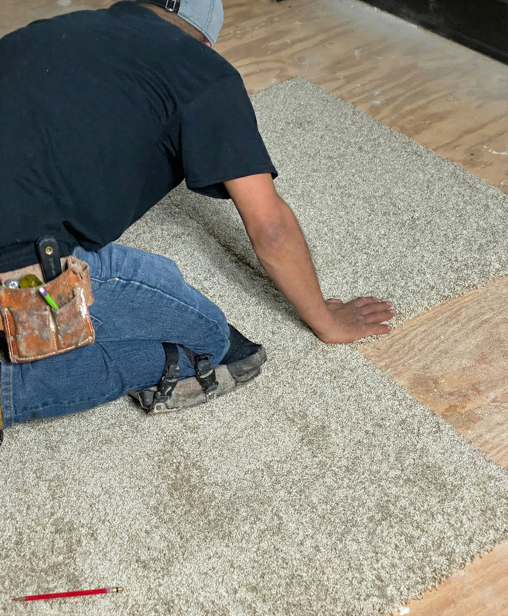 Person installing carpet squares on a wooden floor. 