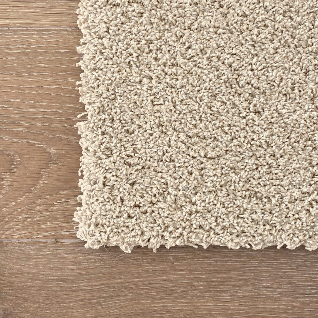 Close-up of a textured beige carpet corner on a wooden floor. Machine washable LCT carpet tiles squares DIY - Washable alternative to peel and stick - soft, plush, pet stain resistant